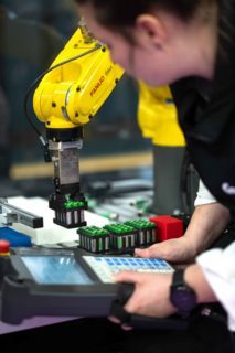 Personnes en train de commander un bras qui place des lots de piles