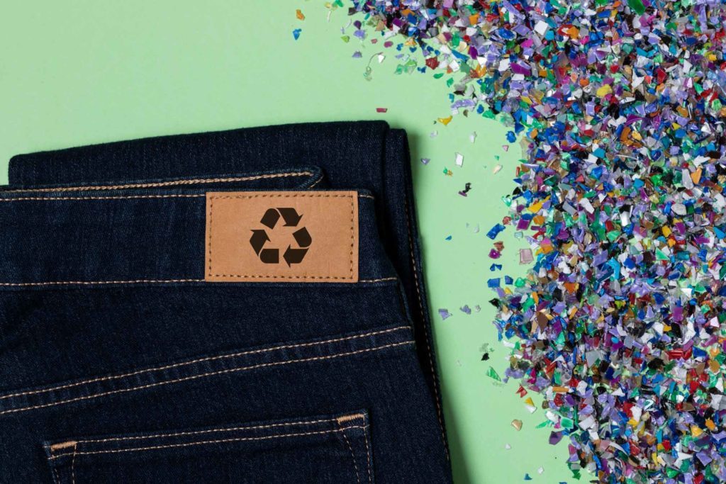 Jean avec le sigle recyclable dessus et des copeaux de plastique multicolores à côté