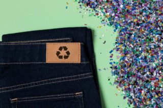 Jean avec le sigle recyclable dessus et des copeaux de plastique multicolores à côté
